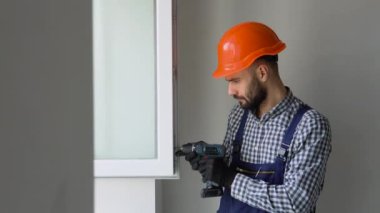 Üniformalı ve kasklı bir tamirci yeni dairedeki PVC pencerelerini tamir ediyor..