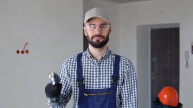 Tulumlu neşeli genç adam ofisinde ya da dairesinde elektrikli matkap tutuyor. Yenileme dairesi için aksesuarlar. Ev konseptini onar.