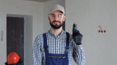 Tulumlu neşeli genç adam ofisinde ya da dairesinde elektrikli matkap tutuyor. Yenileme dairesi için aksesuarlar. Ev konseptini onar.