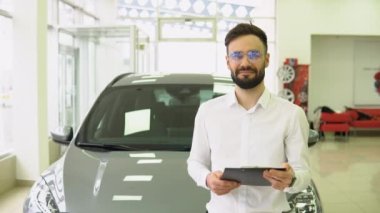 Otomobil Showroom 'daki iş yerinde yakışıklı araba satıcısı pozu, genç bayilik merkezi müdürü ve yeni bir otomobil, ücretsiz alan satın almada yardımcı oluyor.