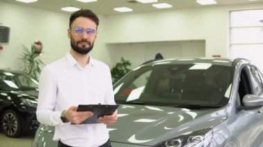 Otomobil Showroom 'daki İş Yeri' nde Yakışıklı Araba Satıcısı Pozisyonu 'nun Portresi, Yeni Otomobil Almaya Yardım Eden Ellerinde Panosu olan Genç Satış Merkezi Müdürü