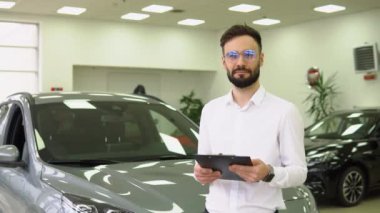 Otomobil Showroom 'daki iş yerinde yakışıklı araba satıcısı pozu, genç bayilik merkezi müdürü ve yeni bir otomobil, ücretsiz alan satın almada yardımcı oluyor.