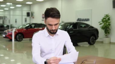 Autodiler satış bürosunda masada otururken bir arabanın satış belgesini imzalıyor.