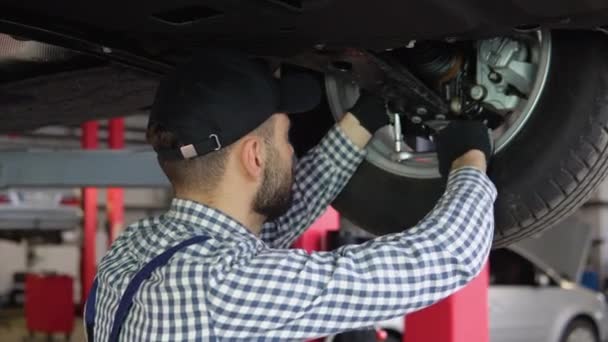 Doświadczony Mechanik Pracujący Pod Samochodem Warsztacie Samochodowym — Wideo stockowe