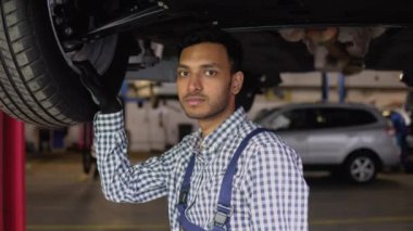 Oto tamir servisinde kaldırılmış arabanın altında çalışan Hintli araba tamircisi. Araba servisi, tamirat.