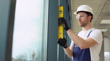 Bir adam pvc pencerelerinin dikey sapmasını ölçer. Kabarcık düzeyi cetvel görünümü, ölçümü ve seviyelendirme kavramını kapat