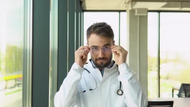 Bonito Jovem Médico Coloca Óculos Olhando Para Câmera Clínica — Vídeo de Stock