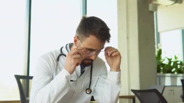 Stresli doktor, beyaz üniformalı, steteskopla yüzünü ellerle kapatan, hastanede çalışma masasında oturan üzgün yaşlı doktor, tıbbi yetersizlikten dolayı kendini çaresiz ve suçlu hissediyor.