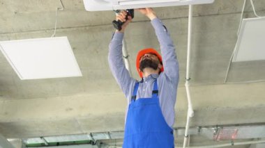 Üniformalı ve kasklı genç işçi ofise klima takıyor..