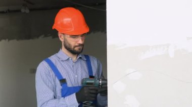 Alçıpan işçisi ya da alçı ustası, kablosuz elektrikli tornavida kullanarak alçı levhaları yeni duvar profillerine yapıştırıyor.