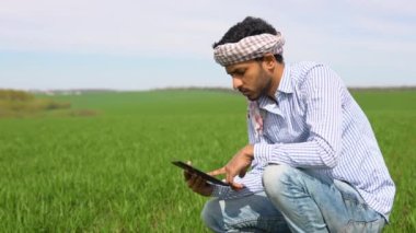 Genç Hintli çiftçi buğday tarlasında çalışıyor, tablet üzerindeki sulama merkezi pivot fıskiye sistemini inceliyor ve ayarlıyor..