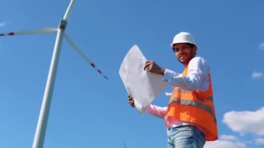 Hint rüzgar türbini mühendisi. Asyalı mühendis rüzgar türbini enerji üretimini yel değirmenlerinin arka planında sürdürüyor ve kontrol ediyor. Sürdürülebilir gelecek kavramı.