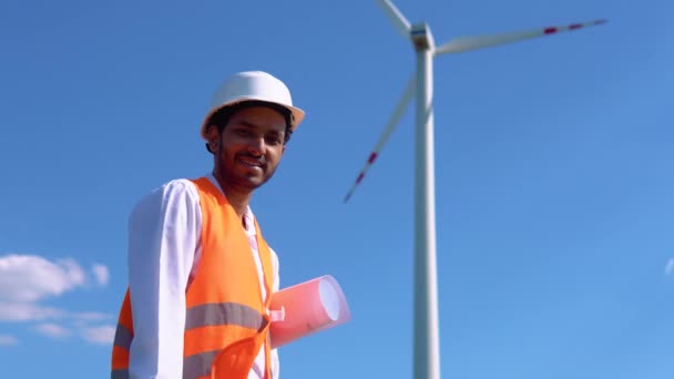 在风力发电场和电线杆旁边微笑的印第安工程师 — 图库视频影像