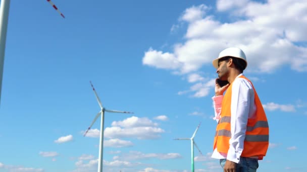 印度工程师坐在一个风力发电厂旁边 在电话里聊天 清洁可再生能源技术 风力发电厂 — 图库视频影像