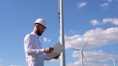 Mühendis rüzgar türbini enerji üretimini yel değirmenlerinin arka planında tutuyor ve kontrol ediyor. Rüzgar türbini mühendisi. Sürdürülebilir gelecek kavramı.