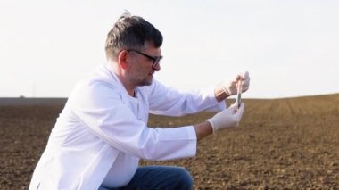 Profesyonel cam taşıyıcısı olan bir laboratuvar çalışanı tarlada hasat yapılmadan önce kara toprağı test ediyor.