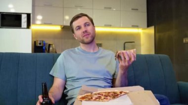 Yakışıklı bir adamın portresi, gece evde bir koltukta oturuyor, TV 'de komedi dizisi izliyor ve pizza yiyor. Man Good Fun İzleme Filmi.