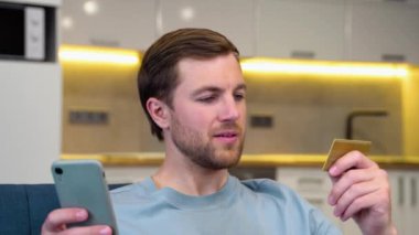 Akıllı telefondan online ödeme yapmak için kredi kartı kullanan bir adam. İnternetten alışveriş yapmak için cep telefonu kullanan beyaz bir adam. Adam uygulamadan kredi kartı işlemlerini kontrol etmek için akıllı telefon kullanıyor..