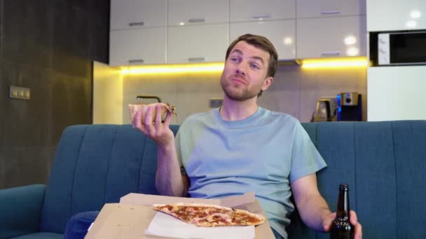 一个英俊男子的画像 他晚上坐在家里的长椅上 在电视上看喜剧系列 吃披萨 男子好好玩观影电影 — 图库视频影像