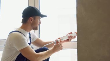 Üniformalı işçi kuşakla pencere çerçevesi arasındaki boşluğu doldurmak için poliüretan köpük uyguluyor. Eviniz için konfor ve konfor yaratıyorsunuz..