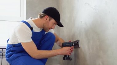 Üniformalı elektrikçi gri duvara elektrik prizleri yerleştiriyor..