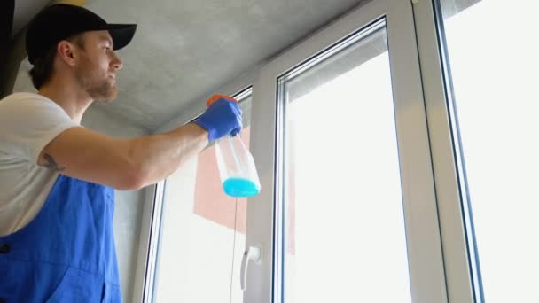 身穿蓝色工作服的年轻人正在打扫公寓的窗户 — 图库视频影像