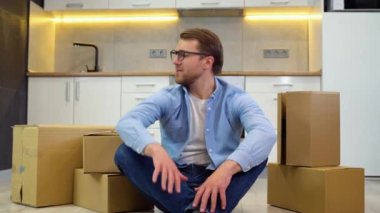 Genç adam yeni evine taşınıyor. Temizledikten ve yerleştirdikten sonra yerde oturup rahatlamak..