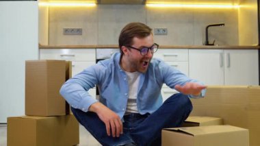 Genç adam yeni evine taşınıyor. Temizledikten ve yerleştirdikten sonra yerde oturup rahatlamak.