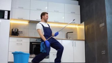 Komik, neşeli, profesyonel temizlikçi paspas tasvirleriyle mola sırasında gitar çalıyor.