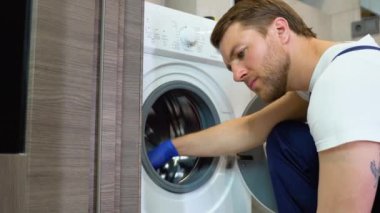 Mavi eldivenli bir adam kirli, küflü lastik bir mührü çamaşır makinesinde temizliyor. Küf, kir, çamaşır makinesinde kireçlenme. Ev aletlerinin düzenli bakımı.