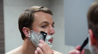 Banyoda tıraş makinesi kullanan kendine güvenen bir adam. Hijyen, cilt bakımı.