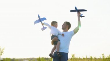 Mutlu aile, çocuk, baba ve uçak gün batımında parkta birlikte oynuyorlar. Evlat, baba pilot olma hayali kuruyor. Takım çalışması baba, çocuk, havacılar. Çocukluk hayalleri uçuyor. Oyuncak uçak elinde, güneşte