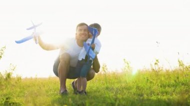 Mutlu aile, çocuk, baba ve uçak gün batımında parkta birlikte oynuyorlar. Takım çalışması baba, çocuk, havacılar. Oyuncak uçak elinde, güneşte.