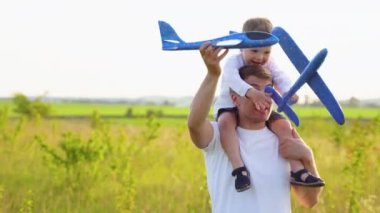 Mutlu aile, çocuk, baba ve uçak gün batımında parkta birlikte oynuyorlar. Takım çalışması baba, çocuk, havacılar. Oyuncak uçak elinde, güneşte.