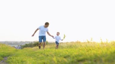 Mutlu baba ve küçük oğlu tarlada güneşte birlikte koşuyorlar. Mutlu aile takımı. Aile oyunu.