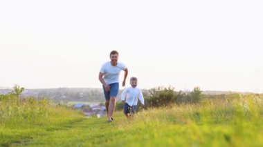 Mutlu baba ve oğul gün batımında çimlerin üzerinde koşar. Arkadaş canlısı aile hayatı.