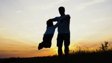 Baba ve oğul gün batımında parkta oynuyorlar. İnsanlar sahada eğleniyor.