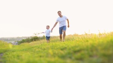 Mutlu baba ve küçük oğlu parkta birlikte koşuyorlar. Mutlu aile takımı. Aile oyunu. Baba oğul eğlence koşusu..