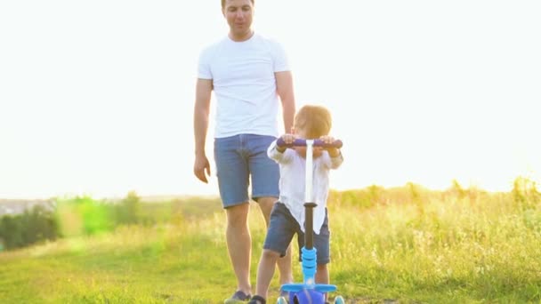 Sonriente Padre Adulto Enseñando Hijo Montar Bicicleta Campo Empujando Scooter — Vídeo de stock