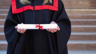 Mezuniyet gününde diploma ya da eğitim diploması tutan üniversite öğrencisinin eli, başarılı eğitim kavramı