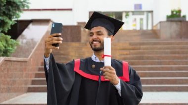 Hintli diplomalı bir öğrenci üniversitenin yanında selfie çekiyor..