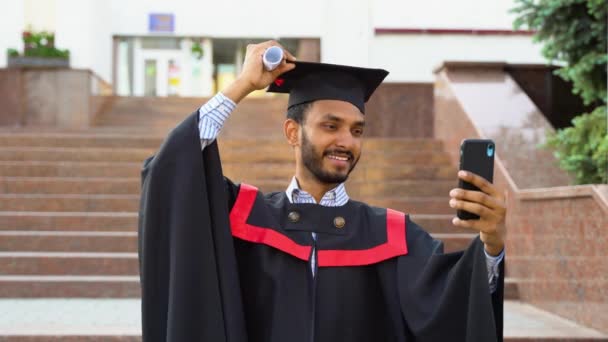 卒業証書付きの自撮り 幸せなインド人学生は卒業の日に幸せになる アジア人男性はスマートフォンを見てセルフィーを作る — ストック動画