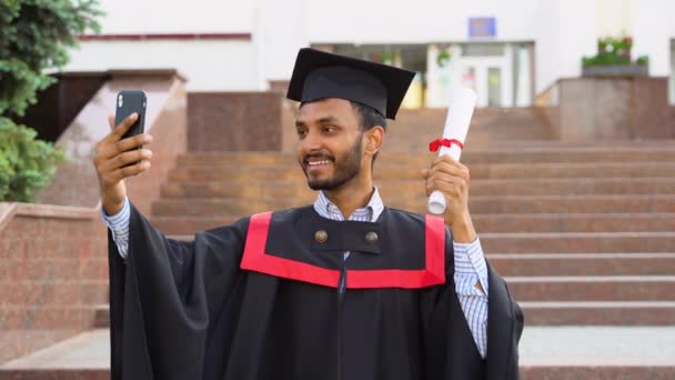 彼は何かを話すと卒業後に彼の卒業証書を手に彼の家族のための自撮りビデオを作るためにカメラを使用してインドの学生卒業生 — ストック動画