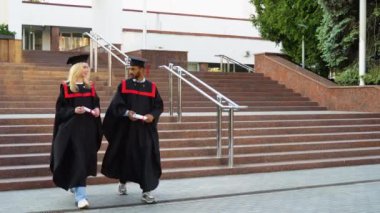 Üniversite kampüsünde yürüyen iki çok ırklı mezun..