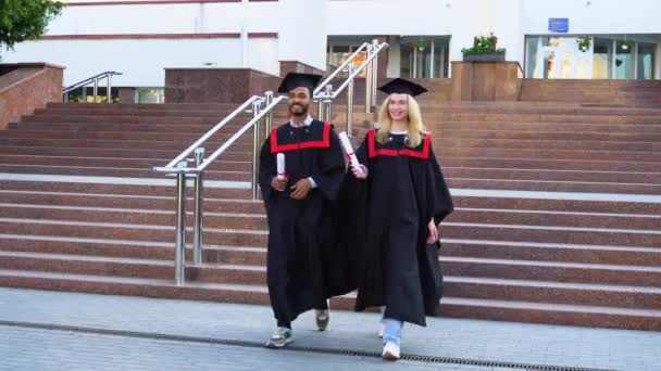 Dos Estudiantes Universitarios Multirraciales Batas Graduación Tableros Mortero Caminando Campus — Vídeo de stock