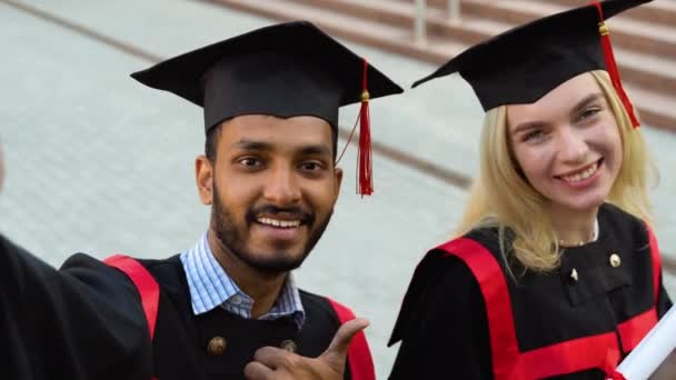 Glückliches Multiethnisches Studentenpaar Abschlussklamotten Und Hüten Das Gemeinsam Ein Selfie — Stockvideo