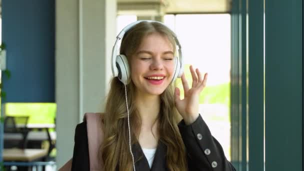 ヘッドフォンで音楽を聴くダンスや歌の女の子の学生 休憩中に大学でイヤホンに立って — ストック動画