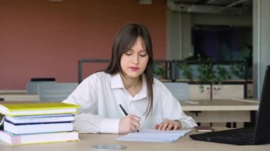 Sınavlar için hazırlanıyor. düşünceli genç kadın Kütüphane masa başında otururken bir şey not defteri ve okuma kitabında yazıyor.