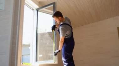 Üniformalı servis elemanı evde mezurayla PVC penceresi kuruyor