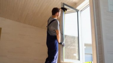 Üniformalı servis elemanı, ahşap prefabrik evde ölçü bandıyla PVC penceresi kuruyor..